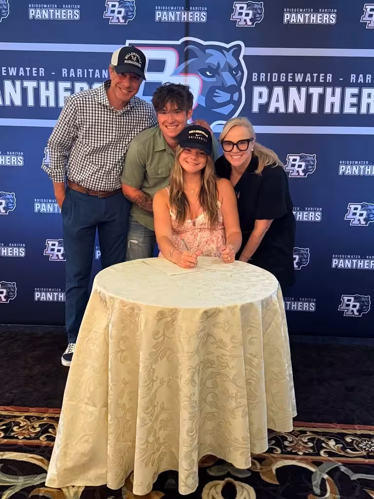 Family signing-day photo against branded step-and-repeat—real-world usage of the identity system during recruiting and recognition events