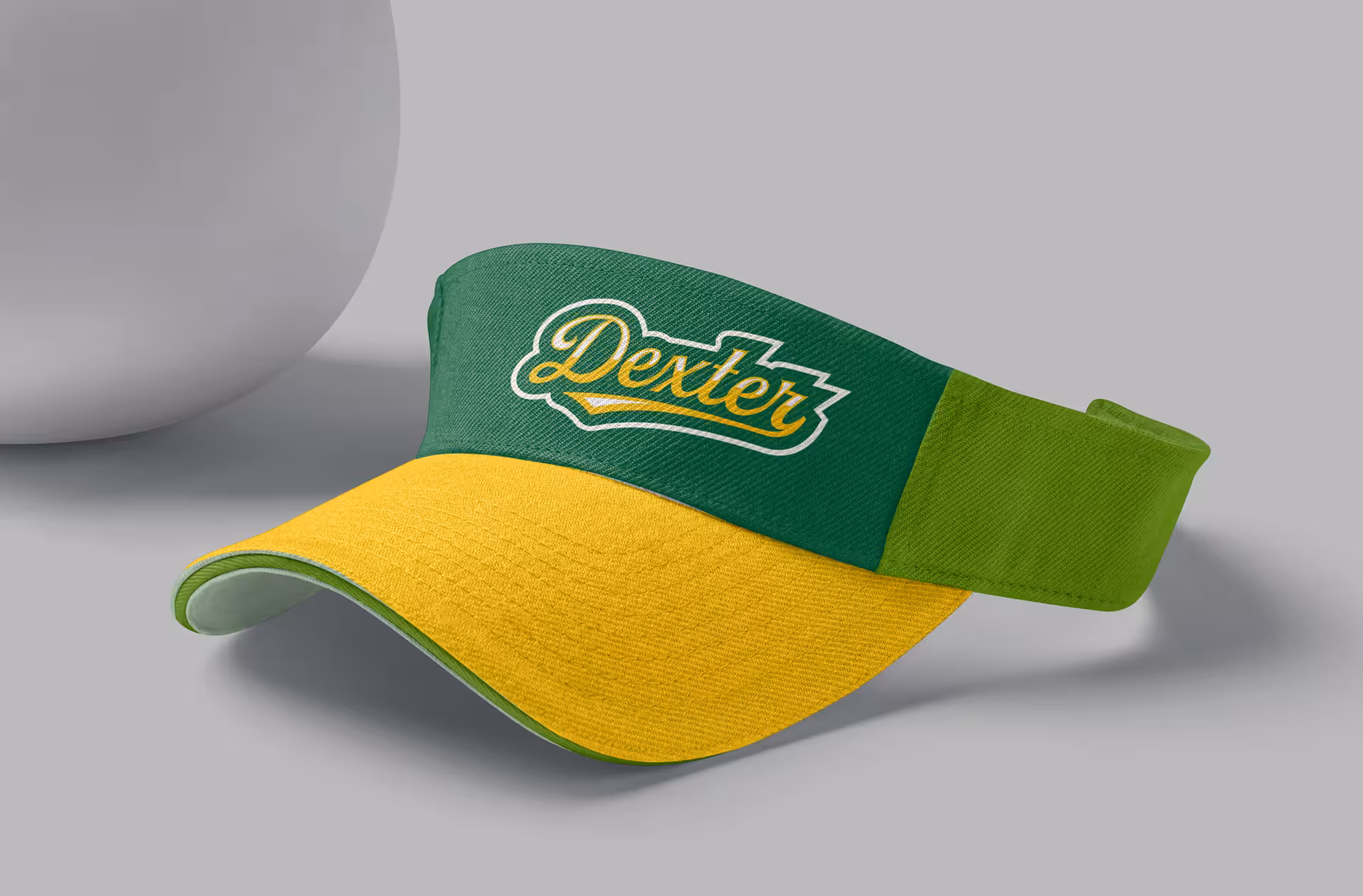 Custom embroidered visor featuring the 'Dexter' script wordmark in two-tone green with gold and white accents, showing the versatility of the brand for athletic merchandise and spirit wear applications
