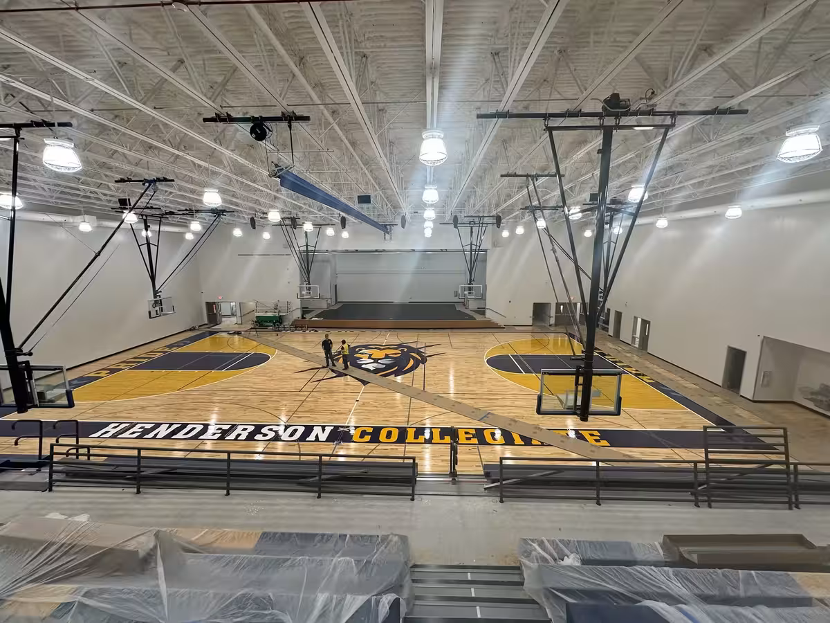 Henderson Collegiate Pride custom basketball court photography showing the complete gymnasium facility with center court lion placement, baseline 'HENDERSON COLLEGIATE' wordmark, sideline 'PRIDE' typography, and distinctive royal blue and gold key areas
